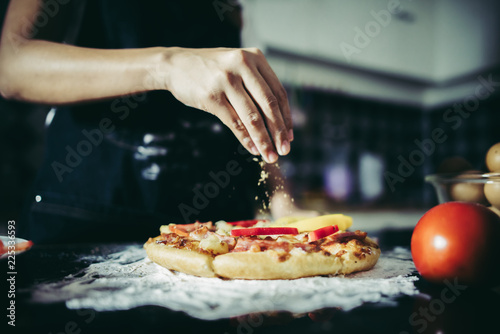 Fototapeta Naklejka Na Ścianę i Meble -  Close up of woman hand putting oregano over tomato and mozzarella on a pizza. Cooking concept