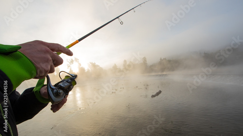 Man fishing in river with fly rod during summer morning.