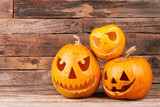 Three Halloween pumpkin heads at sunlight. Halloween pumpkin head jack lantern on wooden background. Traditional Halloween holiday decorations.