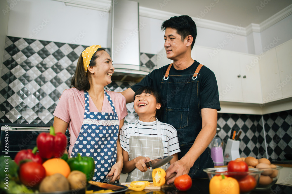 Cute girl help her parents are cutting vegetables and smiling while cooking together in kitchen at home. Cute girl help her parents are cutting vegetables and smiling while cooking together in kitchen at home.