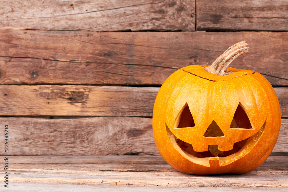 Fototapeta premium Funny Halloween pumpkin on wooden background. Traditional Halloween pumpkin and copy space. Halloween symbols and traditions.