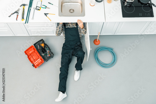 high angle view of plumber lying on floor and checking sink in kitchen photo