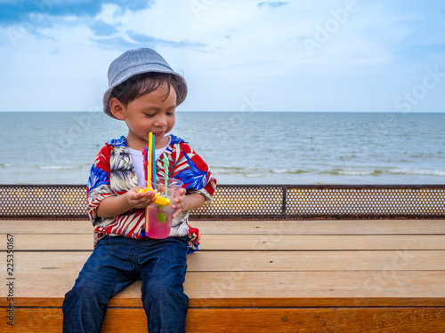 Cute happy asian boy in a summer shirt eating yellow lemon in hand on the wooden table posing background of Hua Hin sea blue skyThailand.Copy-space for your edit. photo