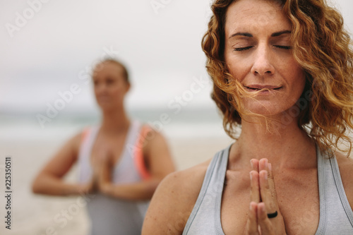 Women in yoga position standing at a beach with joined palms