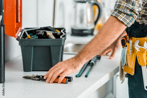 cropped image of plumber putting tools on kitchen counter in kitchen
