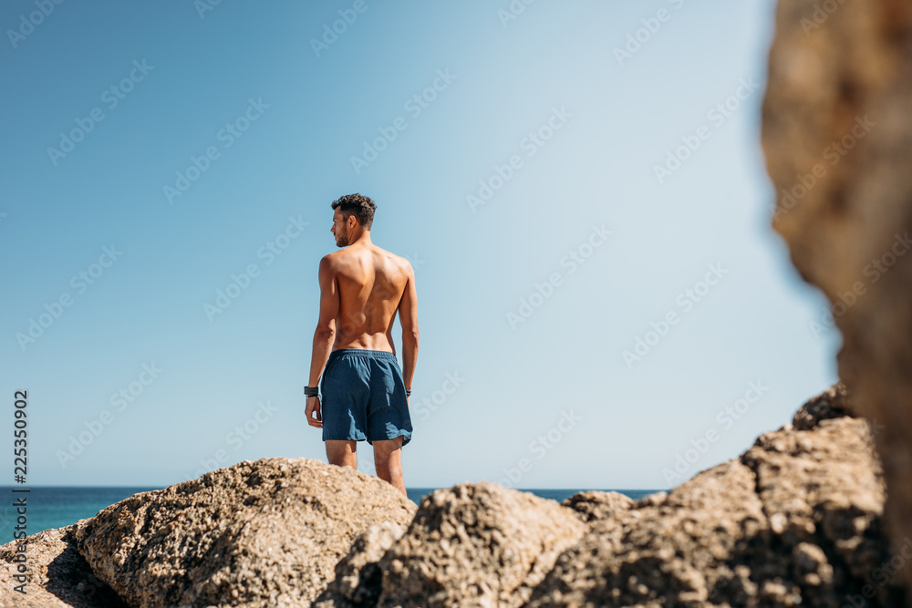 Fototapeta premium Man standing on top of rocks looking at the sea