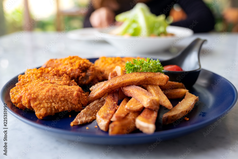 Closeup image of a plate of fried chicken and french fries with a woman eating salad in the restaurant Closeup image of a plate of fried chicken and french fries with a woman eating salad in the restaurant