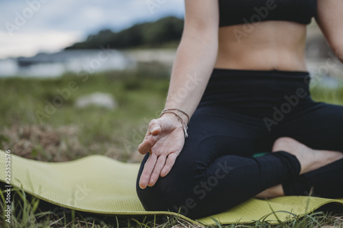 Young beautiful woman doing yoga exercises in park on the bank river in summer