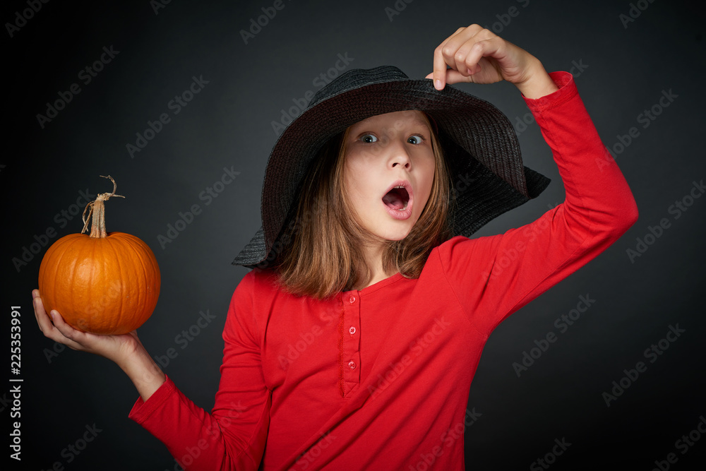 Surprised girl in a black hat holding pumpkin over black background Surprised girl in a black hat holding pumpkin over black background
