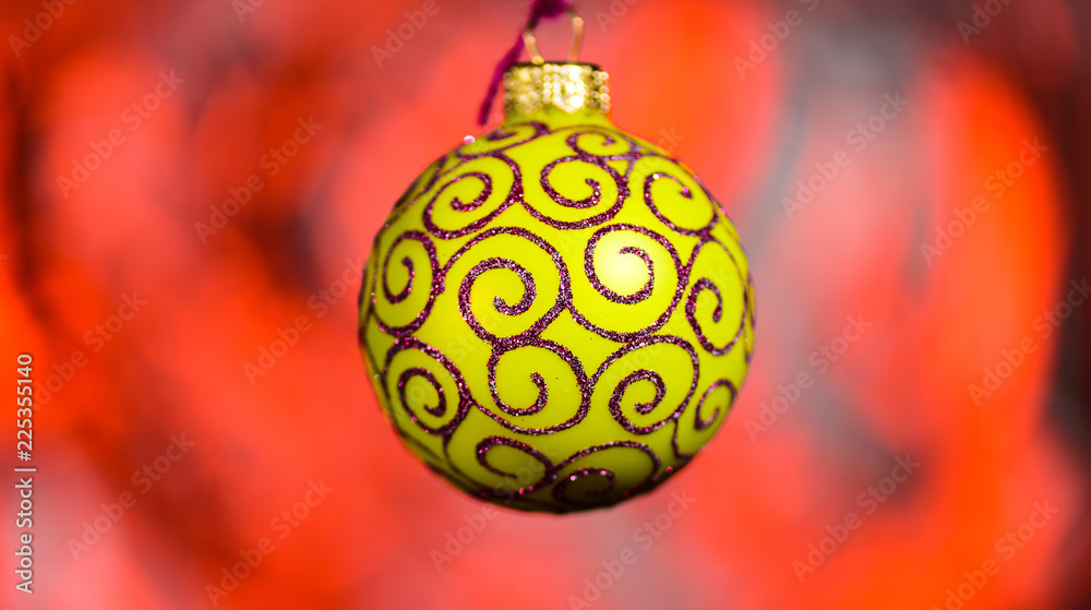 Obraz premium Christmas decoration or toy for Christmas tree with shimmering details. Festive decoration for Christmas tree, yellow ball with glitter decor, on red blurred background. Ornament concept