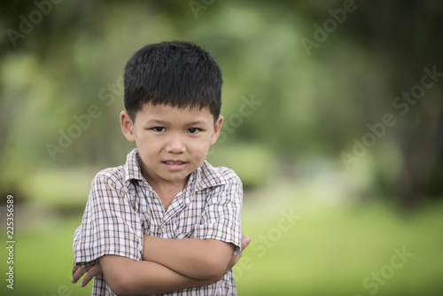 Portrait of cute little curious boy standing with arms folded and looking at camera with blurred nature background.