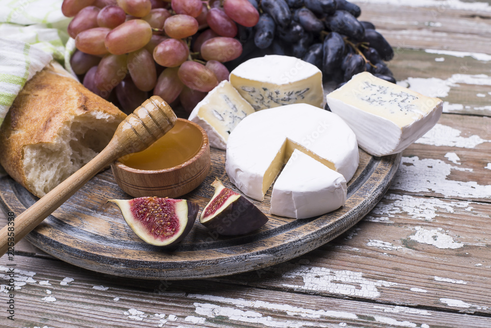 Fresh ripe fruits grape and figs, homemade cheese, honey, white bread on a wooden table.