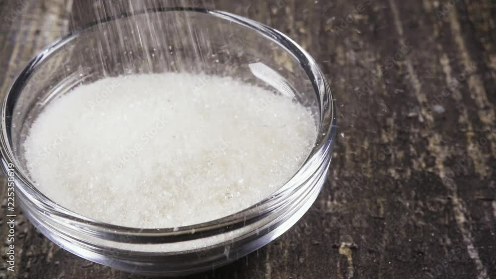 Slow motion pour white sugar into a glass bowl on the table close-up Slow motion pour white sugar into a glass bowl on the table close-up