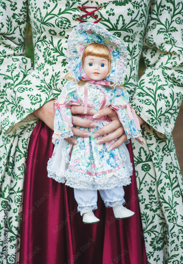 Woman in green medieval dress with vintage porcelain doll