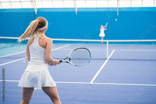 Back view portrait of female tennis player holding racket during training in indoor court, copy space