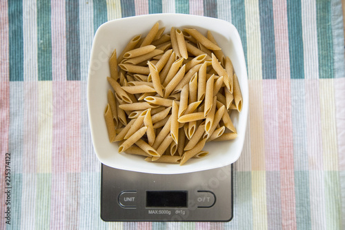 horizontal image with top view of a plate of wholemeal pasta on a digital scale.
