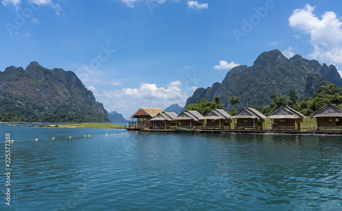 Wooden Thai traditional floating houses on a lake with mountains and rain forest in the background during a sunny day at Ratchaprapha Dam at Khao Sok National Park, Thailand