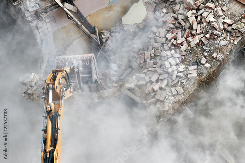 Building demolition with an excavator in dust cloud.