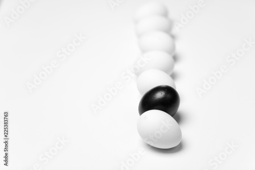 on a white background, white eggs in a row and one black symbolizing diversity, separation, concretion and leadership