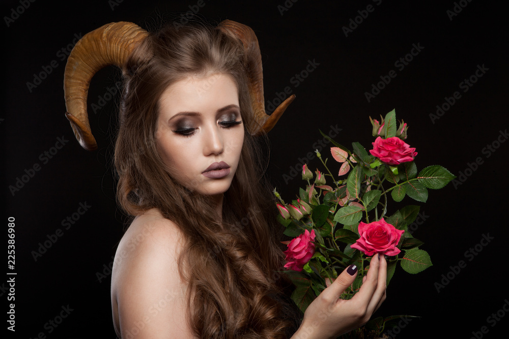 Portrait of an attractive demon woman with horns and curly hair, synthetic flowers, studio shot for Halloween