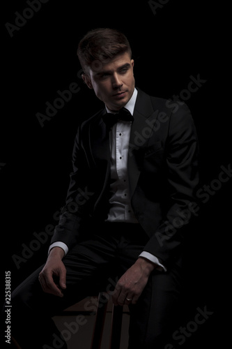 seated stylish man in black tuxedo looks to side