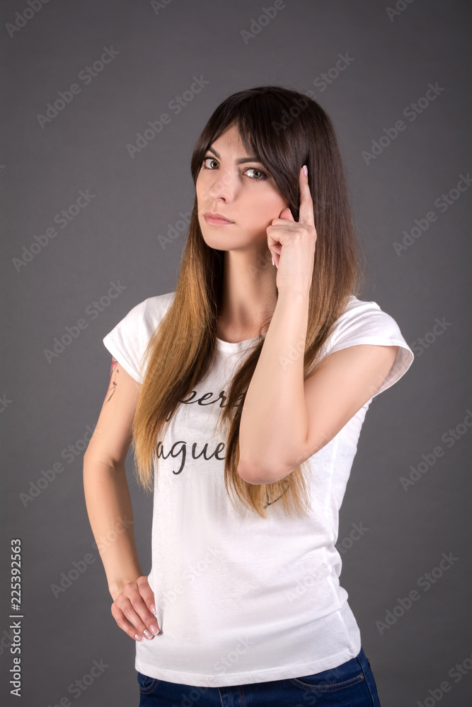 Young woman is thinking about something. Female in a white T-shirt on a gray background. Young woman is thinking about something. Female in a white T-shirt on a gray background.