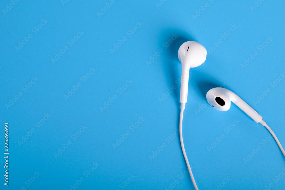 Mobile headphones of white color on a blue background in light colors with a place for text , copyspace. Top view. Mobile headphones of white color on a blue background in light colors with a place for text , copyspace. Top view.