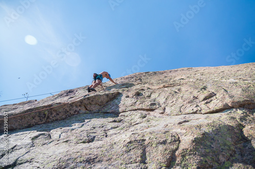 From below shot of shirtless male climber climbing mountain wall on amazing sunny day 