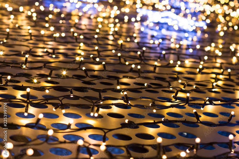 Fototapeta premium Christmas lights of garland on a metal grill with circles, cream color, background.