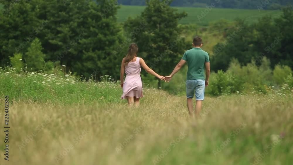 Couple holding hands and walking through the field. Back view Couple holding hands and walking through the field. Back view