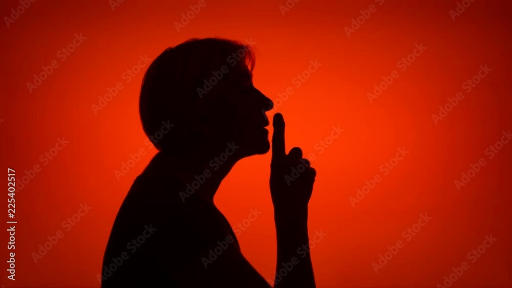 Silhouette of senior woman on red background. Female's face in profile put finger to lips making silence gesture. Black contur shadow of grandmother's half-face shush. Concept of mystery and secrecy Silhouette of senior woman on red background. Female's face in profile put finger to lips making silence gesture. Black contur shadow of grandmother's half-face shush. Concept of mystery and secrecy