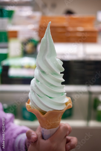 Closeup of female adult holding a cone of delicious and tasty mint softcream or soft serve ice cream made from premium milk. Unhealthy yet enjoy eating concept. Selective focus.