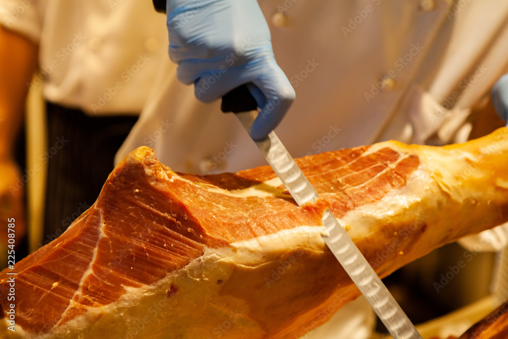 Chef is slicing the whole leg of Spanish Jamon Iberico Ham, made from Black  Iberian pig. Italian Prosciutto Crudo or Parma ham. Tasty and delicious  delicatessen. Popular appetizer or Italian antipasto foto