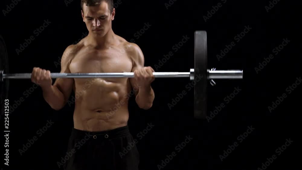 Man is doing exercises with a barbell, training on a black background in the studio Man is doing exercises with a barbell, training on a black background in the studio
