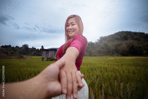 Woman turning and smiling while holding your hand in paddy field.