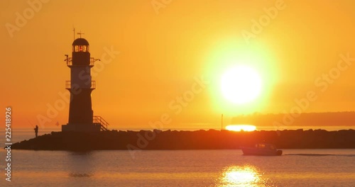 Fisherman next to a lighthouse and a passing boat in Rostock Warnem√ºnde during sunrise photo