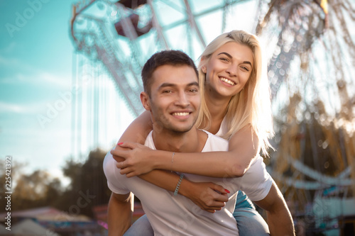Happy young cheerful loving couple walking outdoors in the amusement park having fun.