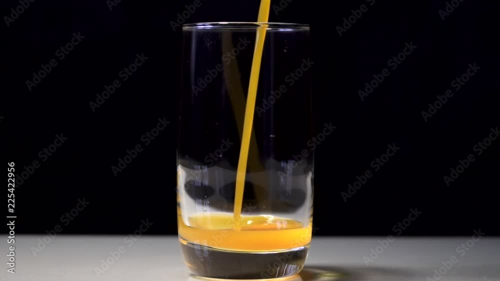 Pouring orange and yellow juice into a glass beaker. Behind the black