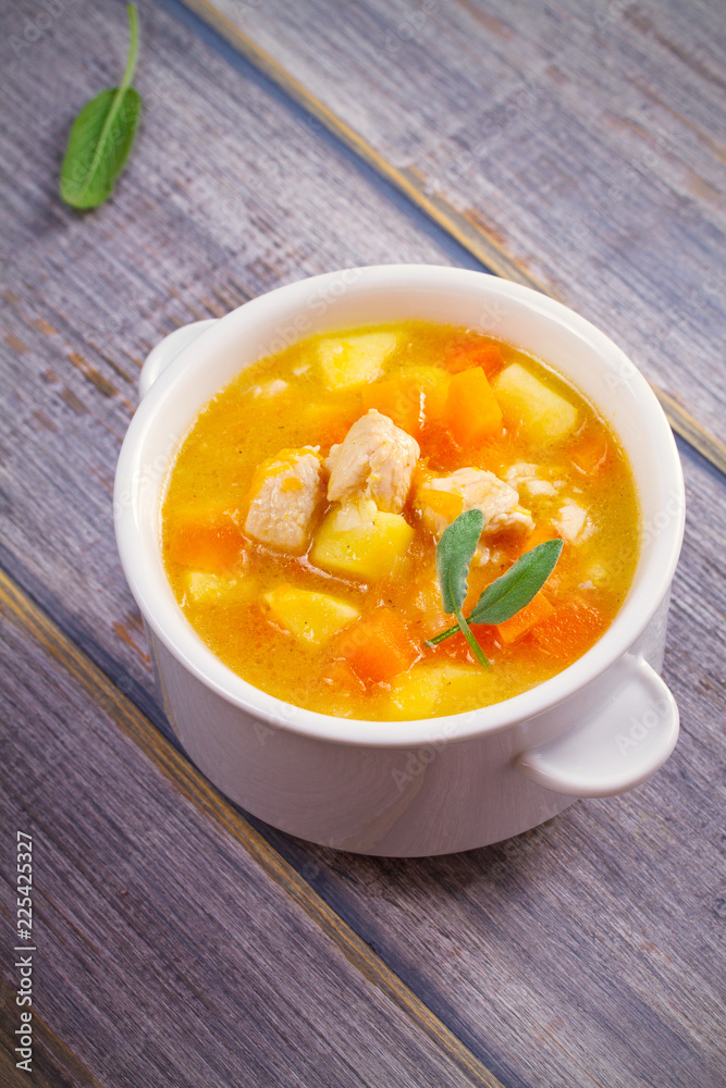 Chicken, butternut squash, apple, ginger and sage stew in white bowl on wooden table. Pumpkin soup with chicken. vertical Chicken, butternut squash, apple, ginger and sage stew in white bowl on wooden table. Pumpkin soup with chicken. vertical