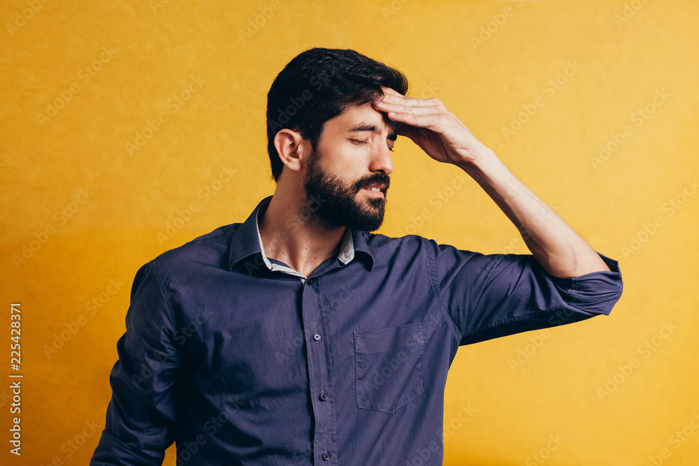 Portrait of an annoyed middle aged man suffering from a headache isolated over yellow background