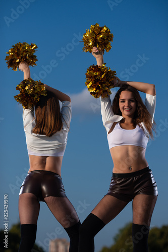 Two girls cheerleaders with pompons dancing outdoors