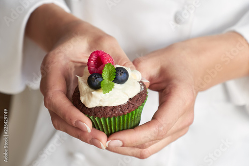 Close-up on hands of female pastry chef with decorated cupcake photo