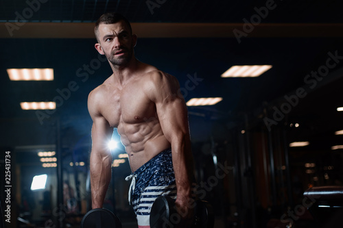 young muscular man posing with dumbbells in hand at the gym