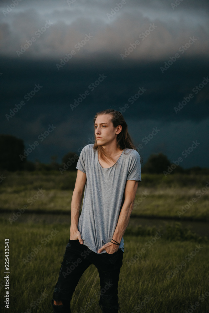 Obraz premium Attractive Young Male Model with Man Bun and Long Blonde Hair Posing for Camera Outside in Filed During Sunset