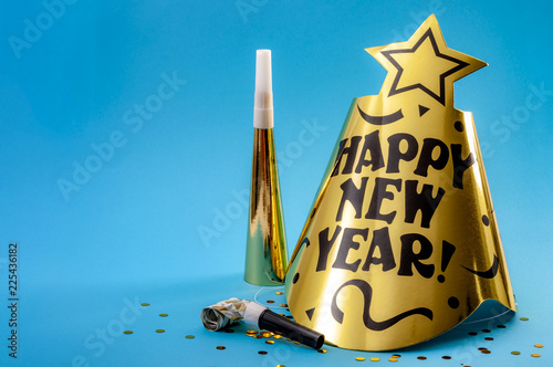 Happy new year concept with a festive hat, noisemakers, confetti, party blower  and paper trumpet isolated on blue background with copy space