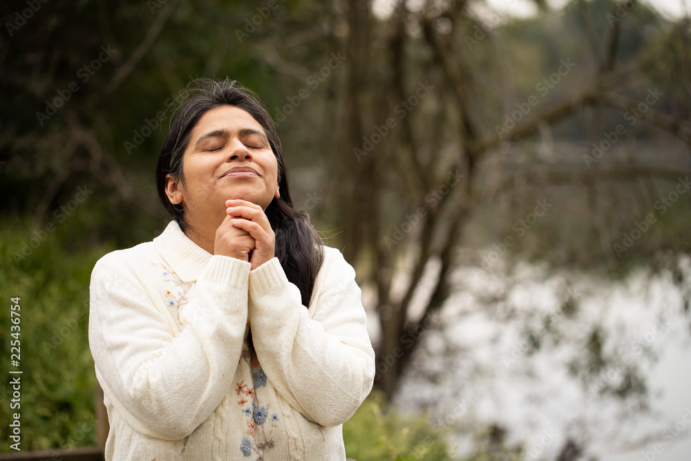 Hispanic Woman Praying in Forest Preserve Front of River
