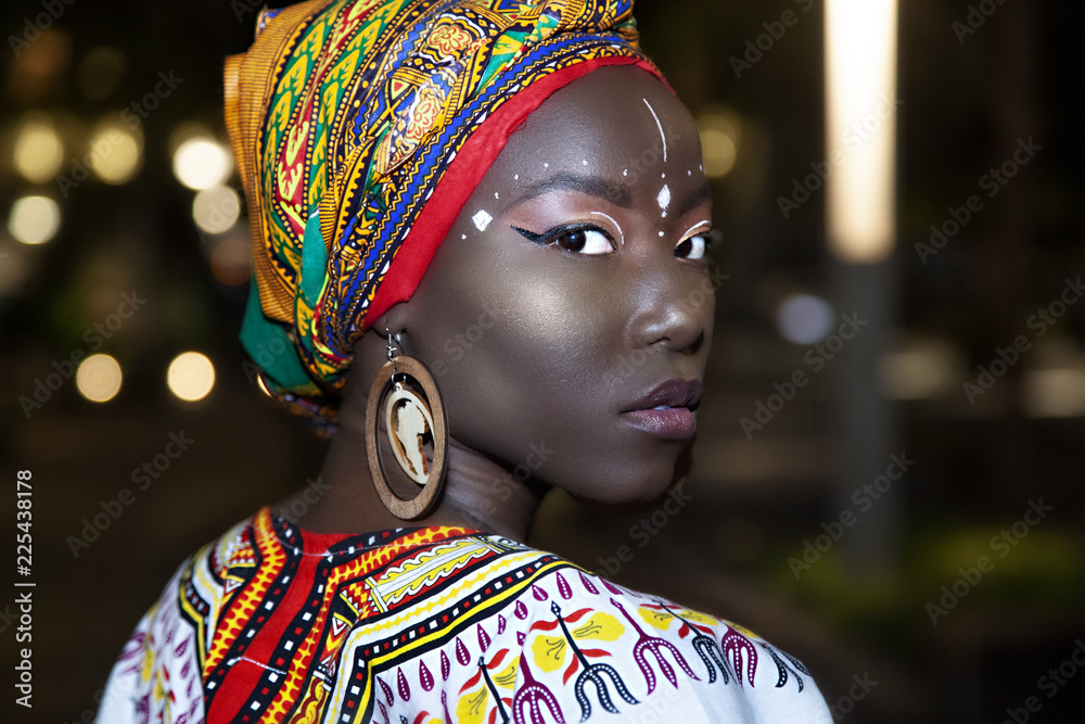 young Jamaican woman wearing traditional African clothes and style makeup  highlighting her amazing rich culture. the color scheme is very bright with  rich dark tones. shot in Chicago at night Stock Photo