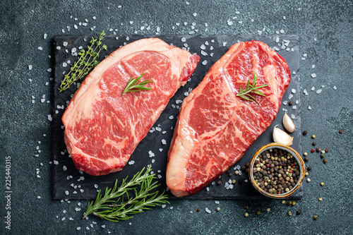 Fresh raw Prime Black Angus beef steaks on stone board: Striploin, Rib Eye. Top view. On a dark background