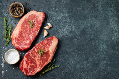 Fresh raw Prime Black Angus beef steaks on stone board: Striploin, Rib Eye. Top view with copy space. On a dark background
