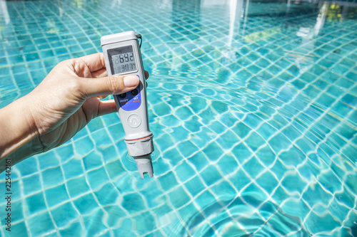 Digital waterproof and temp pocket tester in girl hand over blue swimming pool water, water tester, outdoor day light photo